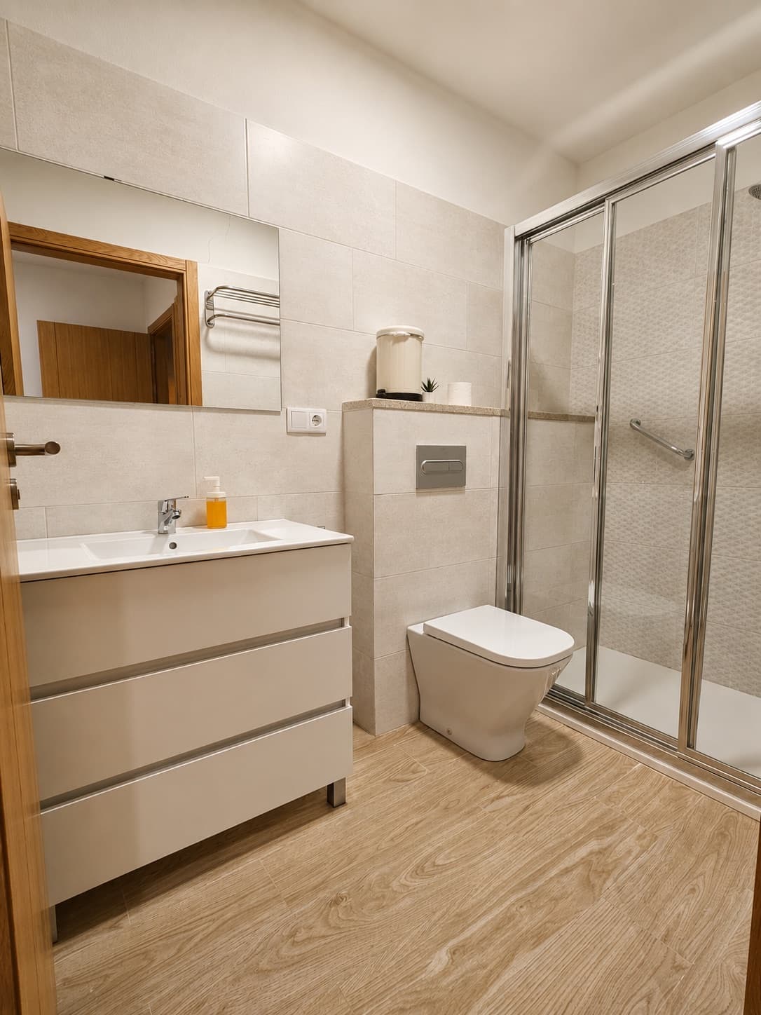 Baño con ducha de obra, mampara de cristal y suelo de madera