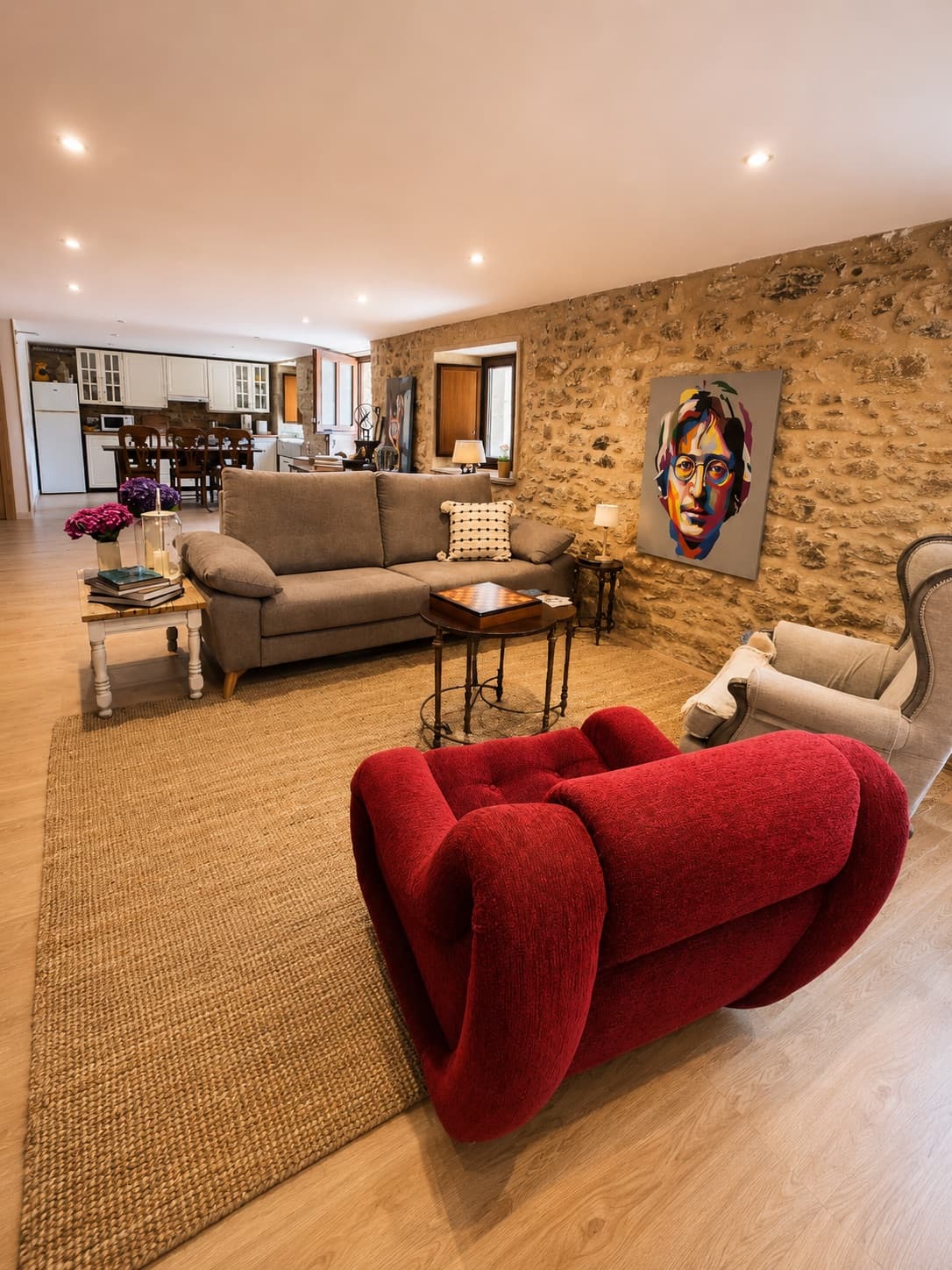 Salón con sofás, sillón de diseño y muro de piedra, abierto a la cocina